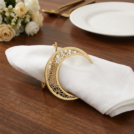 Decorative gold napkin ring on a white napkin with flowers and cutlery in the background.