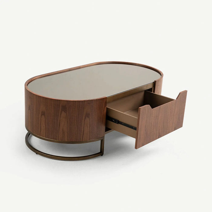An oval mid-century modern coffee table with a dark walnut wood finish, a glass top, and an open drawer showing a bronze pull handle, set against a plain off-white background.