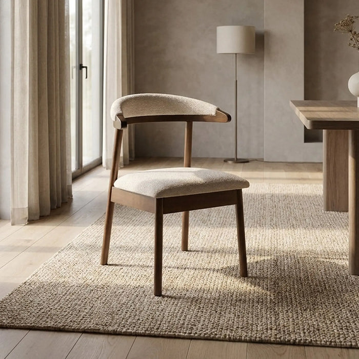 A mid-century modern accent chair with a curved wooden backrest and light beige textured upholstery, styled on a woven jute rug in a bright, neutral-toned room.