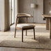 A mid-century modern accent chair with a curved wooden backrest and light beige textured upholstery, styled on a woven jute rug in a bright, neutral-toned room.