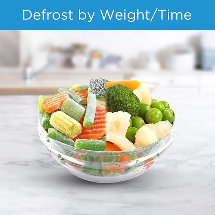 Frozen vegetables in a glass bowl with text 'Defrost by Weight/Time' on a blurred kitchen background.