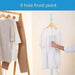 Person using a garment steamer on a white shirt with clothes on a rack in the background.