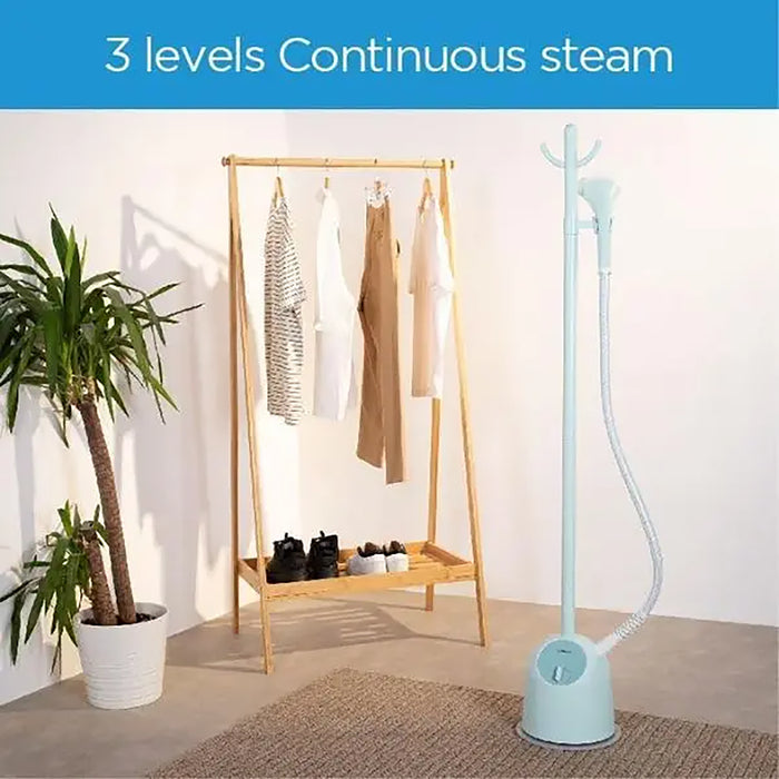 Light blue garment steamer next to a wooden clothing rack with clothes in a room setting.