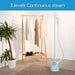 Light blue garment steamer next to a wooden clothing rack with clothes in a room setting.