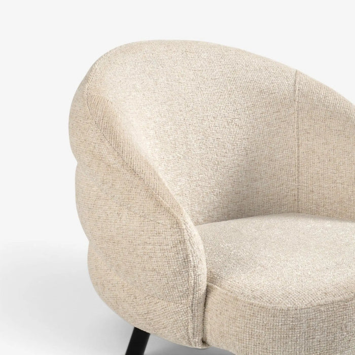 Close-up of a modern upholstered accent chair with a rounded, cloud-like back and seat in a textured beige fabric, set against a clean white background.
