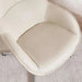 A close-up of a modern upholstered chair in warm off-white leather, showing the seat cushion and curved armrests, with a textured light rug underneath.