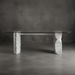 Glass dining table with marble legs against a dark gray wall.