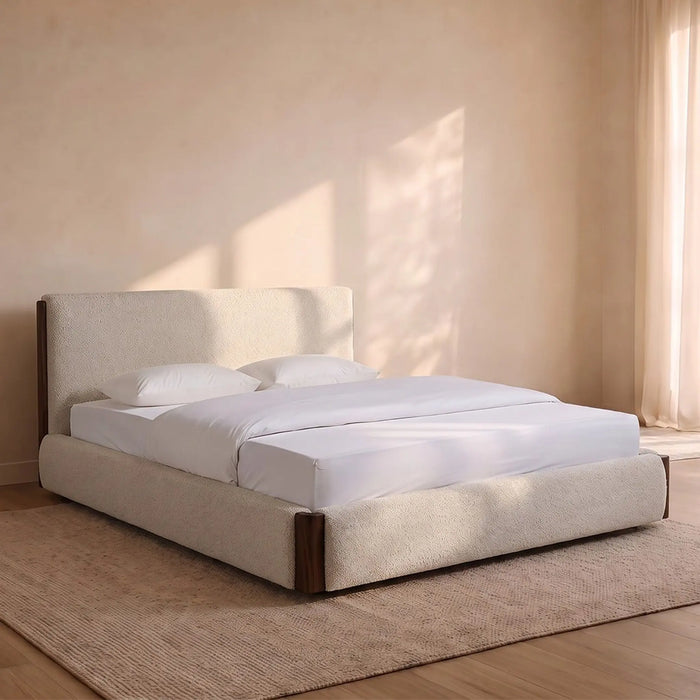 A modern platform bed with a tall upholstered headboard and matching base, dressed in white bedding, set in a softly lit bedroom with a beige rug and warm sunlight on the wall.