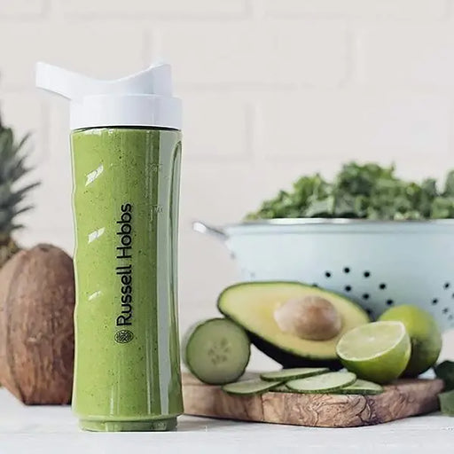 Green smoothie in a Russell Hobbs cup with avocado, lime, and cucumber on a wooden board.