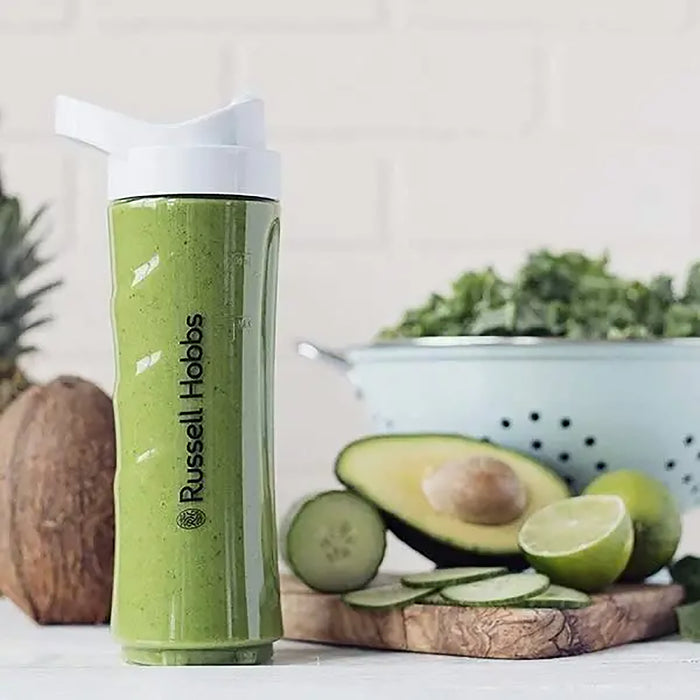 Green smoothie in a Russell Hobbs cup with avocado, lime, and cucumber on a wooden board.